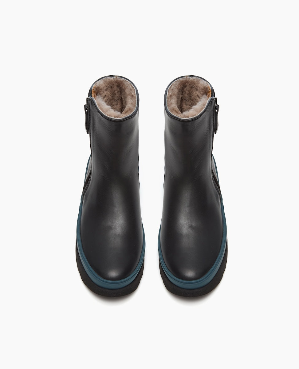 Black ankle boots with a smooth leather exterior, blue trim around the sole, a rounded toe, and a plush, fur-lined interior.