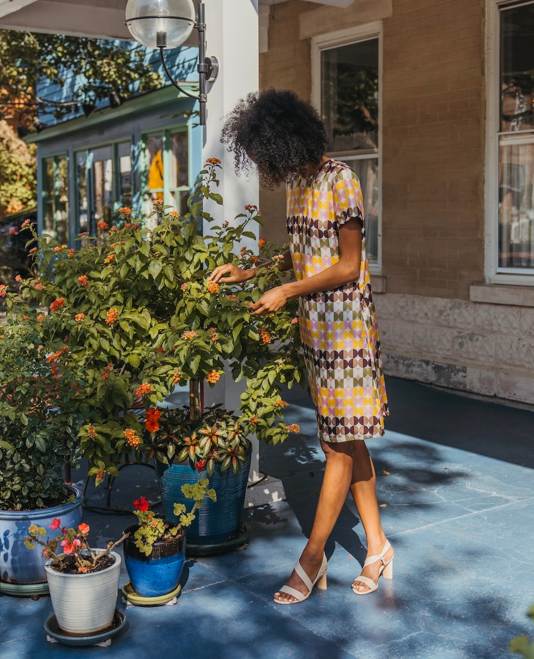 Woman standing outside touching plants and wearing a printed shift dress with the Gabby Heel in Latte Macchiato.