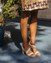 Legs of a woman wearing the Gabby Heel in Latte Machiatto with a printed dress and a plant to the left.  6