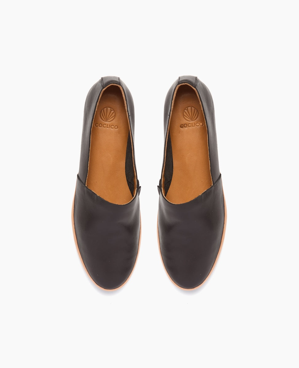 A pair of sleek, black leather slip-on shoes with a smooth texture, rounded toe, tan interior, and a subtle logo embossed on the insole.