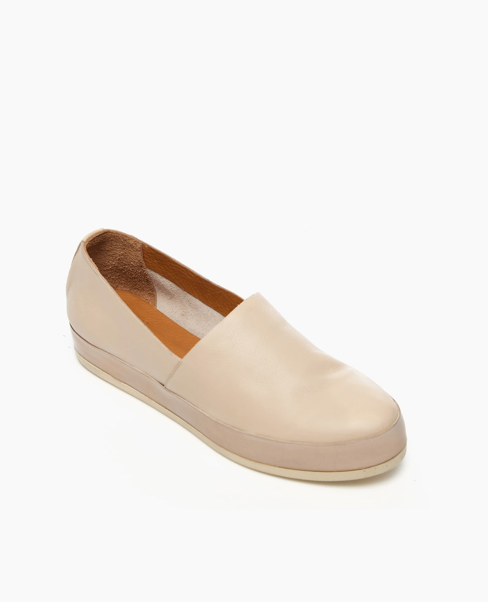 A beige slip-on shoe with a smooth leather upper, rounded toe, and a flat, slightly elevated rubber sole.