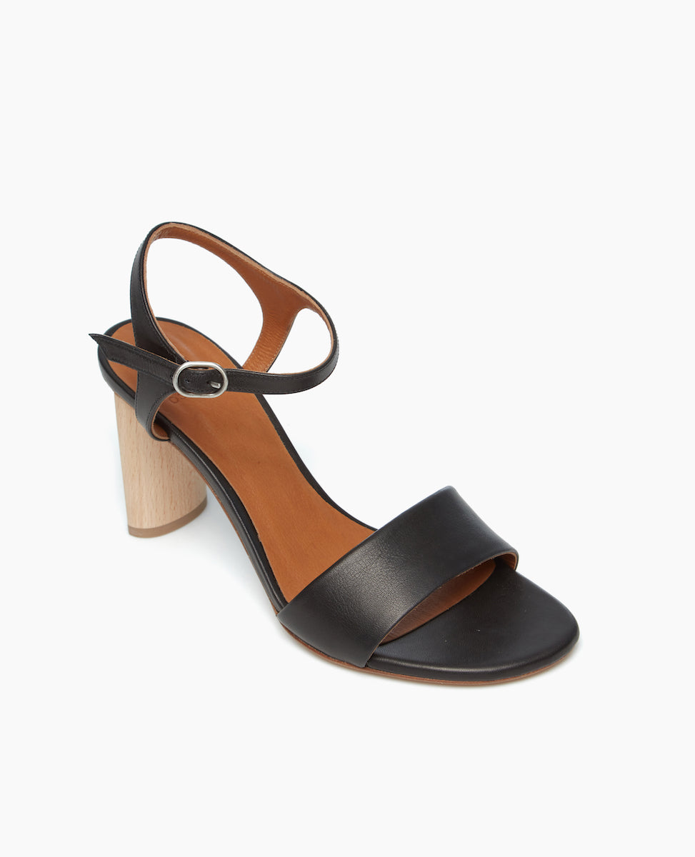 Angled view of the Gigi Heel in black leather with a crisp quarter strap upper with a buckle closure and heel sculpted from solid Ash wood.