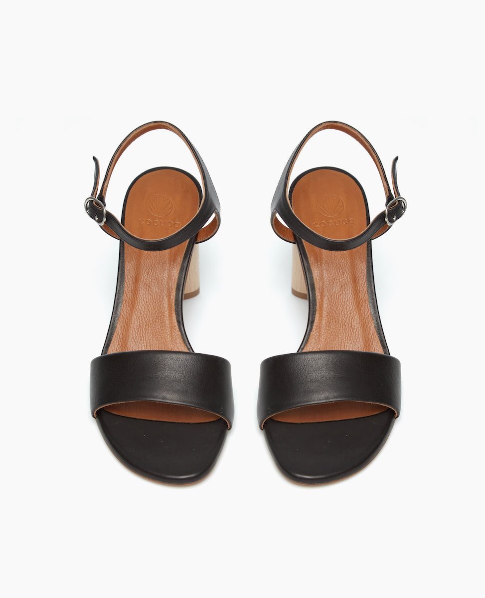 Front view of the Gigi Heel in black leather with modern, minimal features such as a crisp quarter strap wtih a buckle closure.