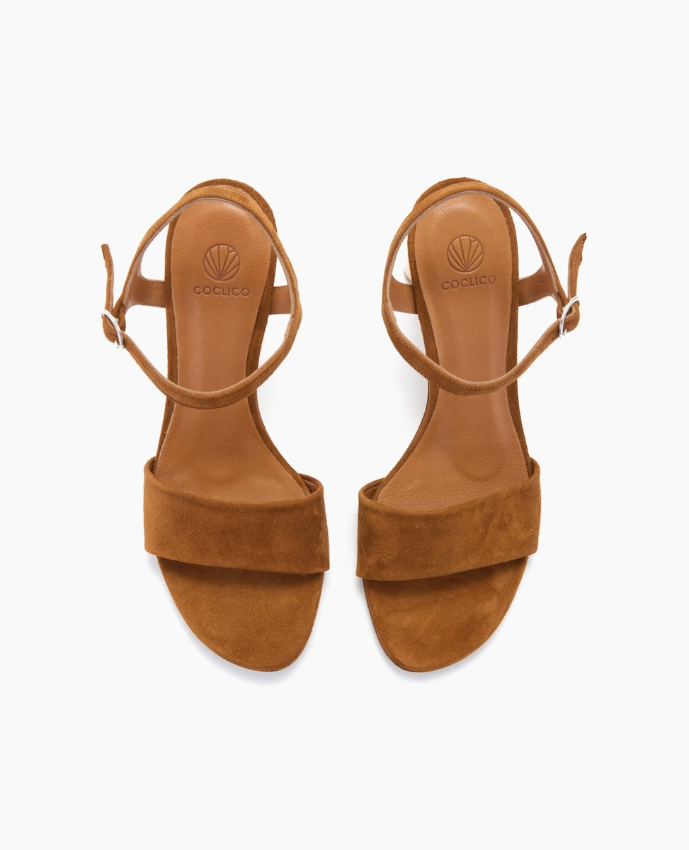Brown suede sandals with a smooth leather insole, featuring a wide front strap, an adjustable ankle strap with a small buckle, and a flat sole.