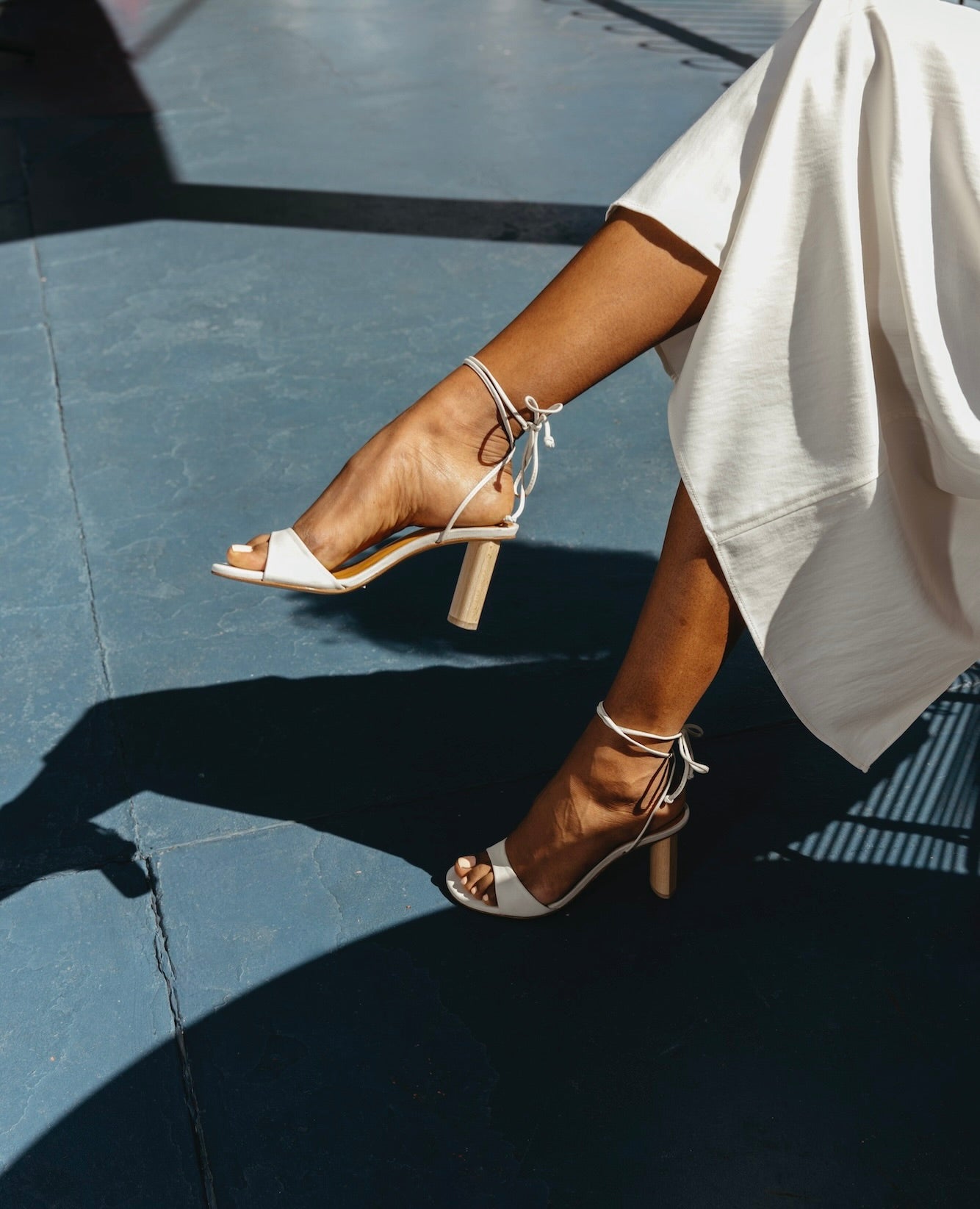 Legs and feet wearing the Gilda in Griege Nubuck with the right knee crossed over the left and a grey skirt draped around the knees.