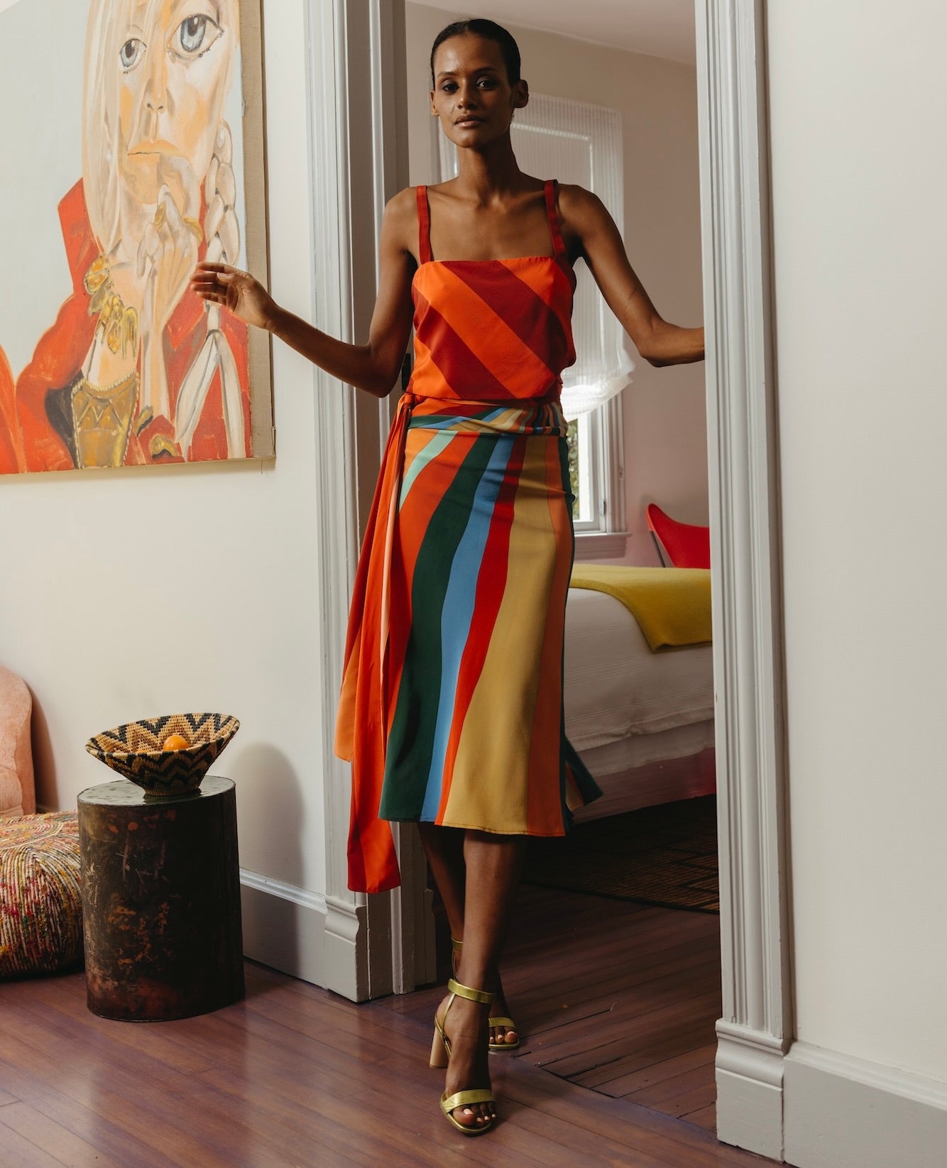 Woman standing in a doorway wearing a rainbow dress with the Gina Heel in Chartreause Antiqued Patent.