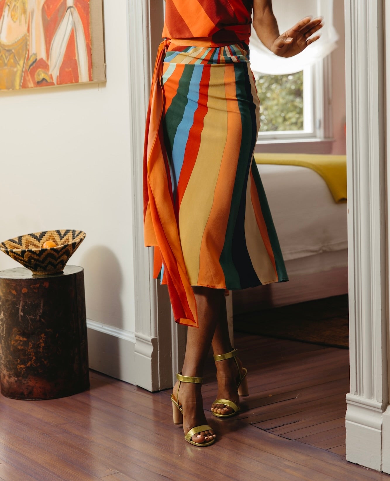 Lower half of a woman standing in a doorway wearing a rainbow dress and the Gina Heel in Chartreause.