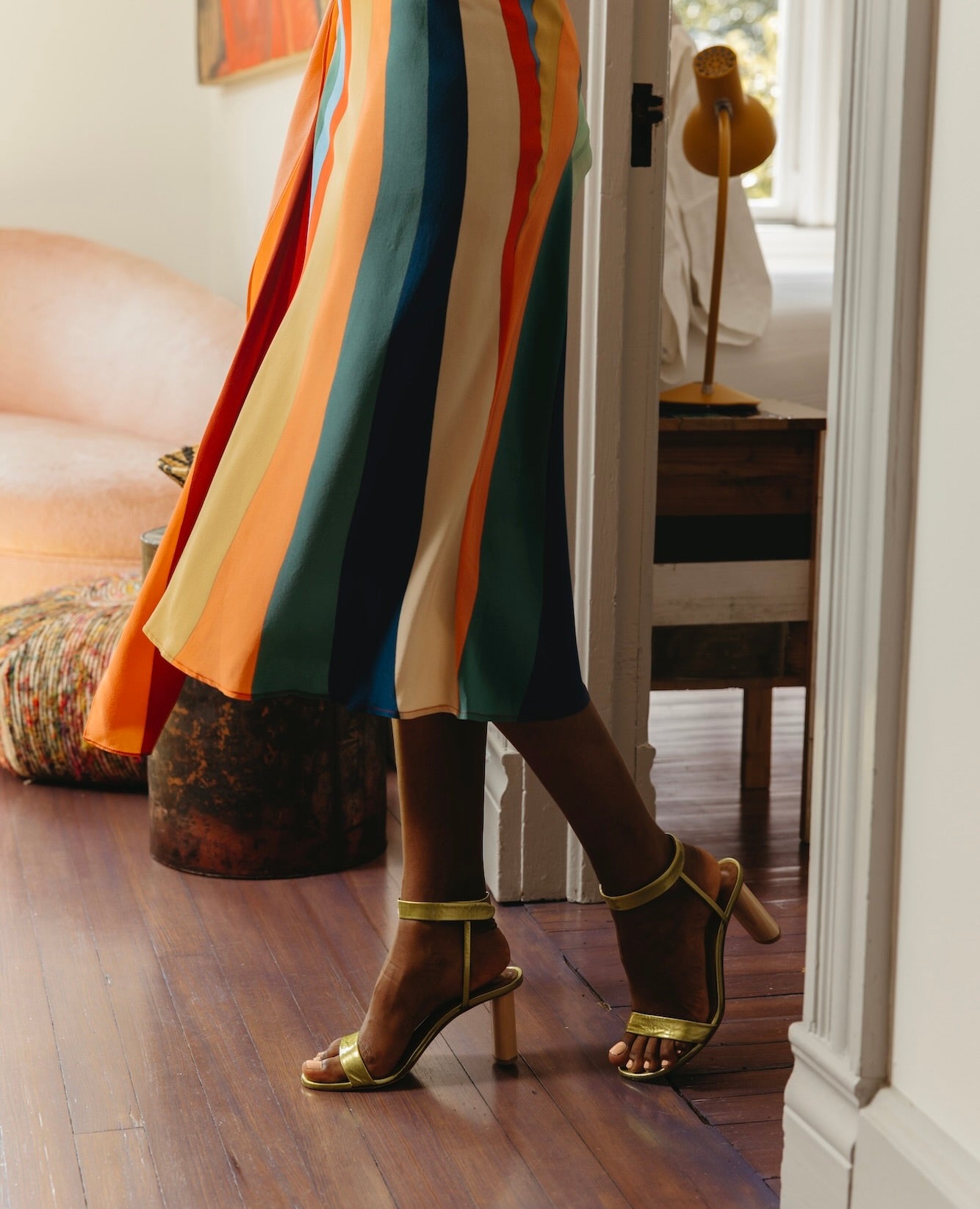 Side view of a woman standing in a doorway wearing a rainbow dress with the Gina Heel in Chartreause.