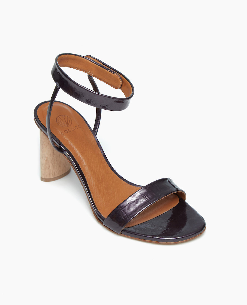 Angled view of the Gina Heel in Black Pearl Patent featuring a straight, narrow front strap and ankle strap that is secured with velcro for a supportive and seamless look as well as an artfully sculpted heel.