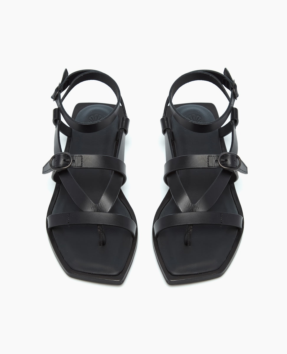 A pair of sleek black leather sandals featuring a square toe design, adjustable ankle straps with buckles, and a minimalist, smooth finish.