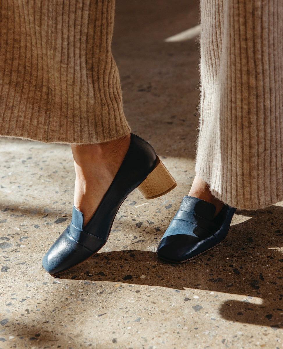 A pair of navy blue leather shoes with a sleek design, featuring a low, chunky wooden heel and a smooth, polished finish.