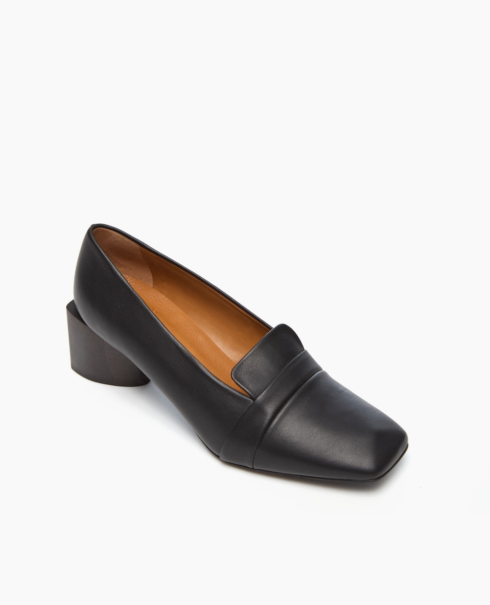 A sleek black leather loafer with a square toe, low block heel, and smooth finish, featuring a minimalist design and a tan interior lining.