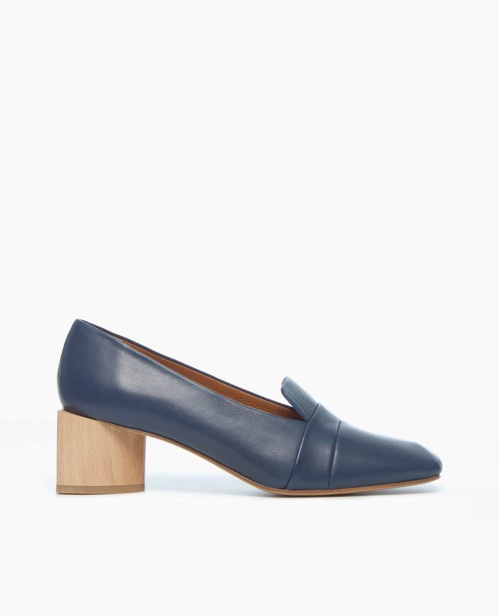 A sleek, navy blue leather shoe with a low, chunky wooden heel and a smooth, rounded toe.