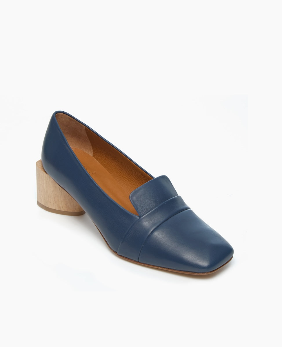 A blue leather loafer with a square toe, featuring a low, chunky wooden heel and a smooth, polished finish.