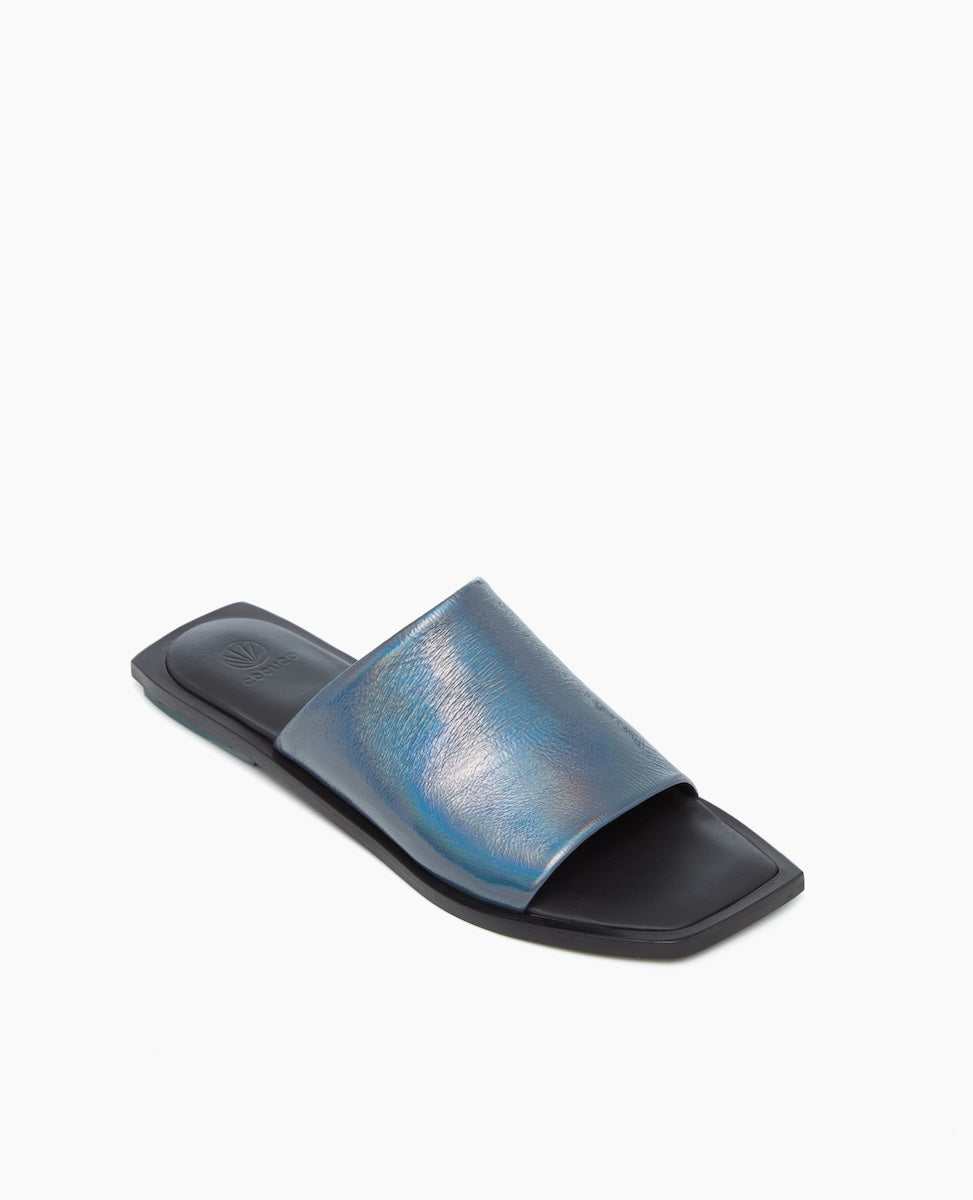 A sleek, black slide sandal featuring a wide, iridescent blue strap with a subtle sheen, a flat sole, and a minimalist design.