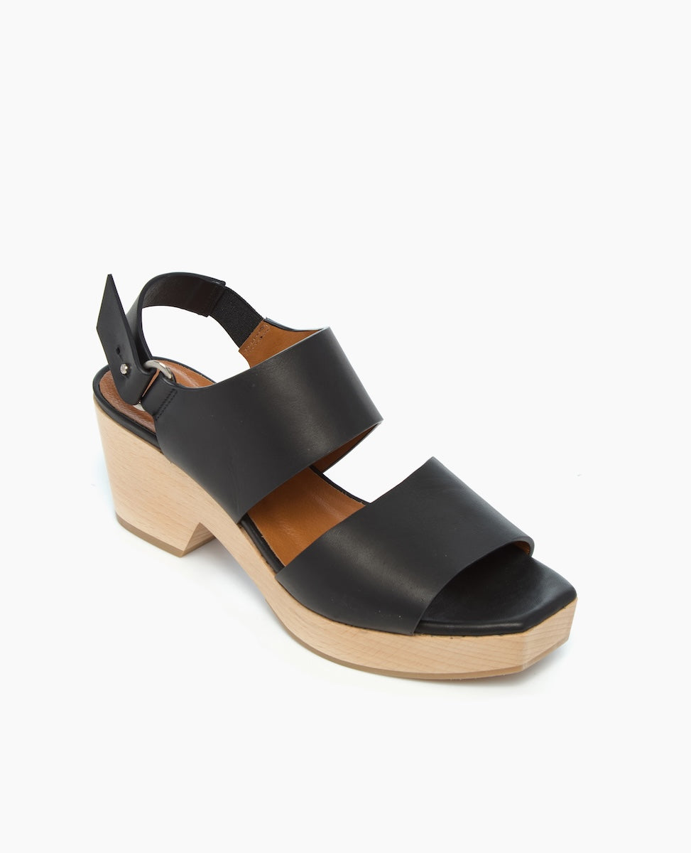 A black leather sandal with two wide straps, an adjustable ankle buckle, and a chunky light wooden block heel.