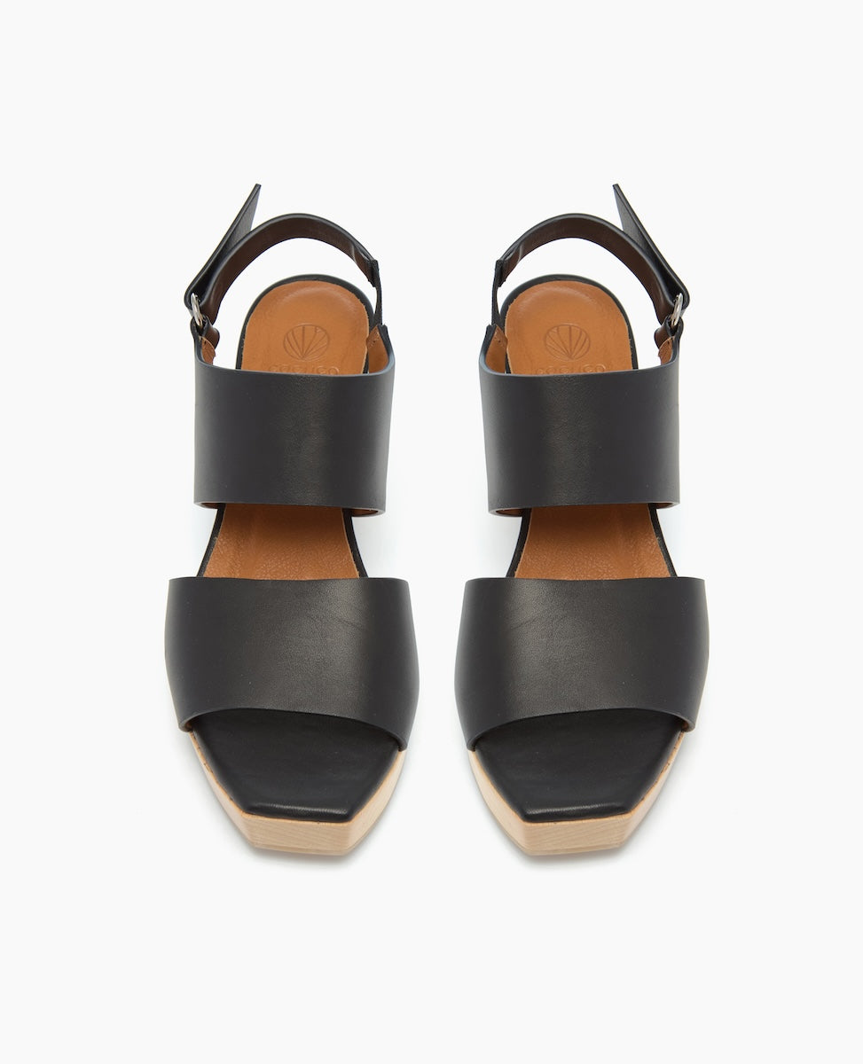 Black leather sandals with wide straps, a tan insole, a square open toe, and a buckle closure at the ankle.
