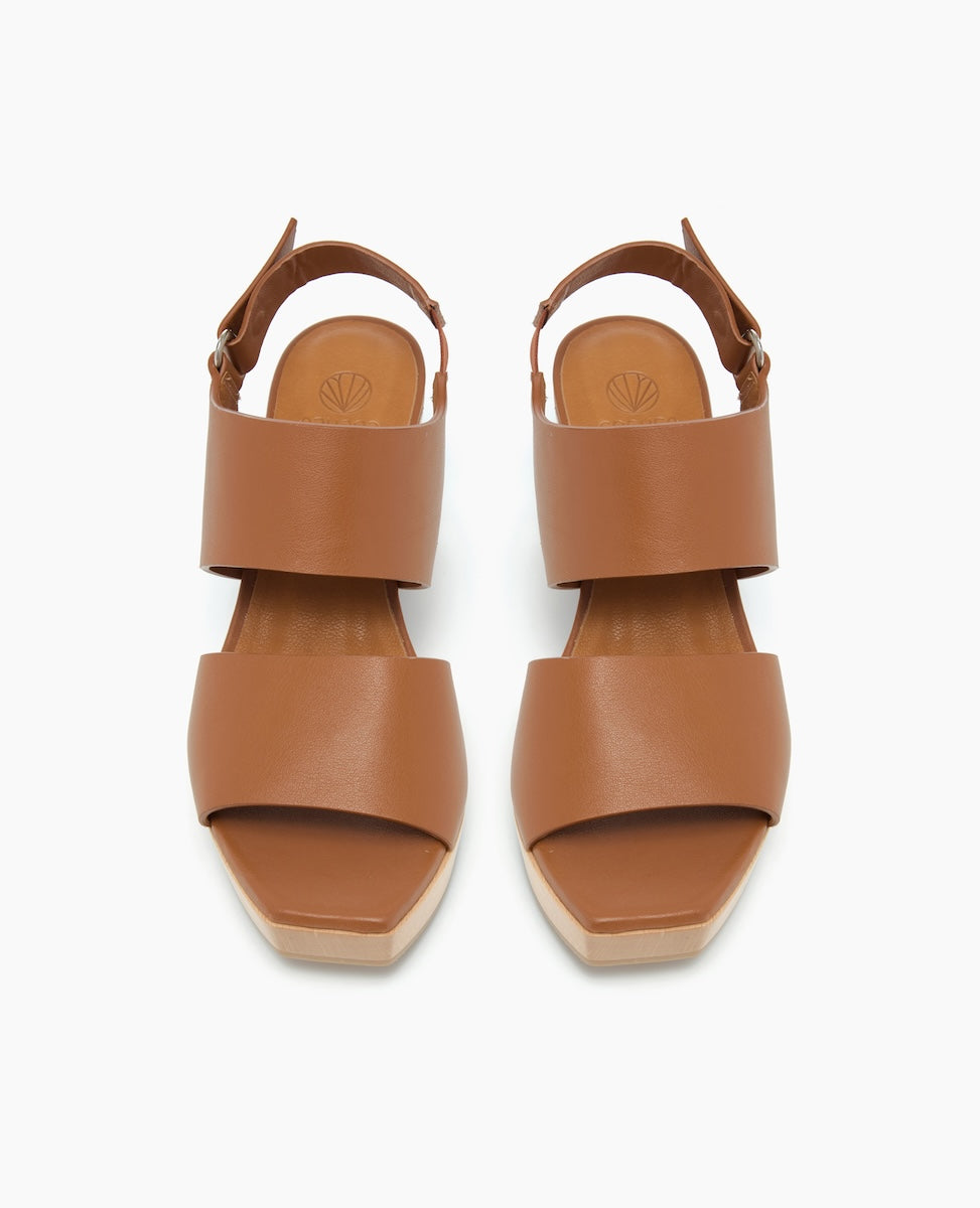 Brown leather sandals with wide straps, a closed back, and a flat, light-colored sole.