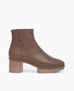 Side view of the Nigella Clog in Taupe leather. Set on a solid wood heel and platform, the midsole is rounded and completely unique, with a simple, clean bootie silhoute. Side tab. Inside-zip closure. 1