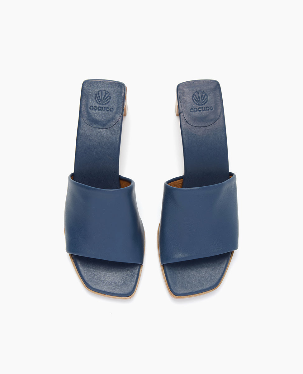 A pair of blue leather sandals with a wide strap across the foot, featuring a square toe design and a subtle logo imprint on the insole.