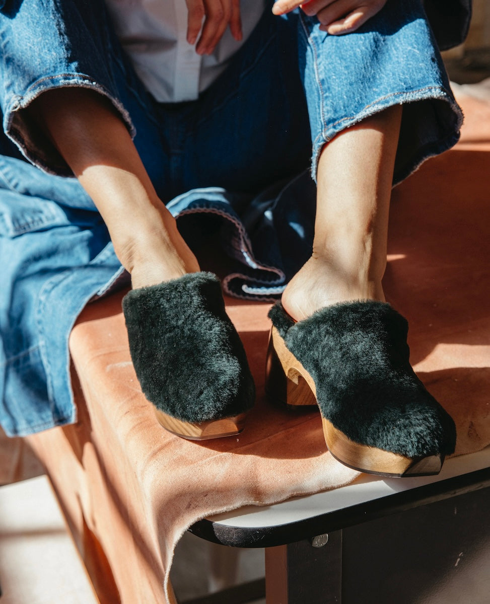 Hunter Green Shearling slip-on clogs with wooden soles worn by a person in blue denim pants.