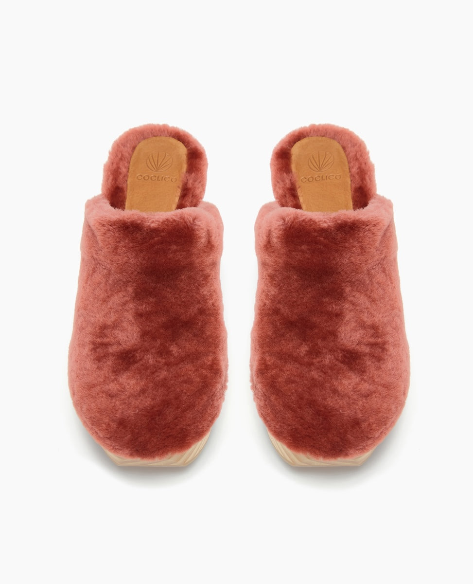 Plush, rust-colored slippers with a soft, fuzzy texture, featuring a closed-toe design, a tan leather insole, and a flat sole.