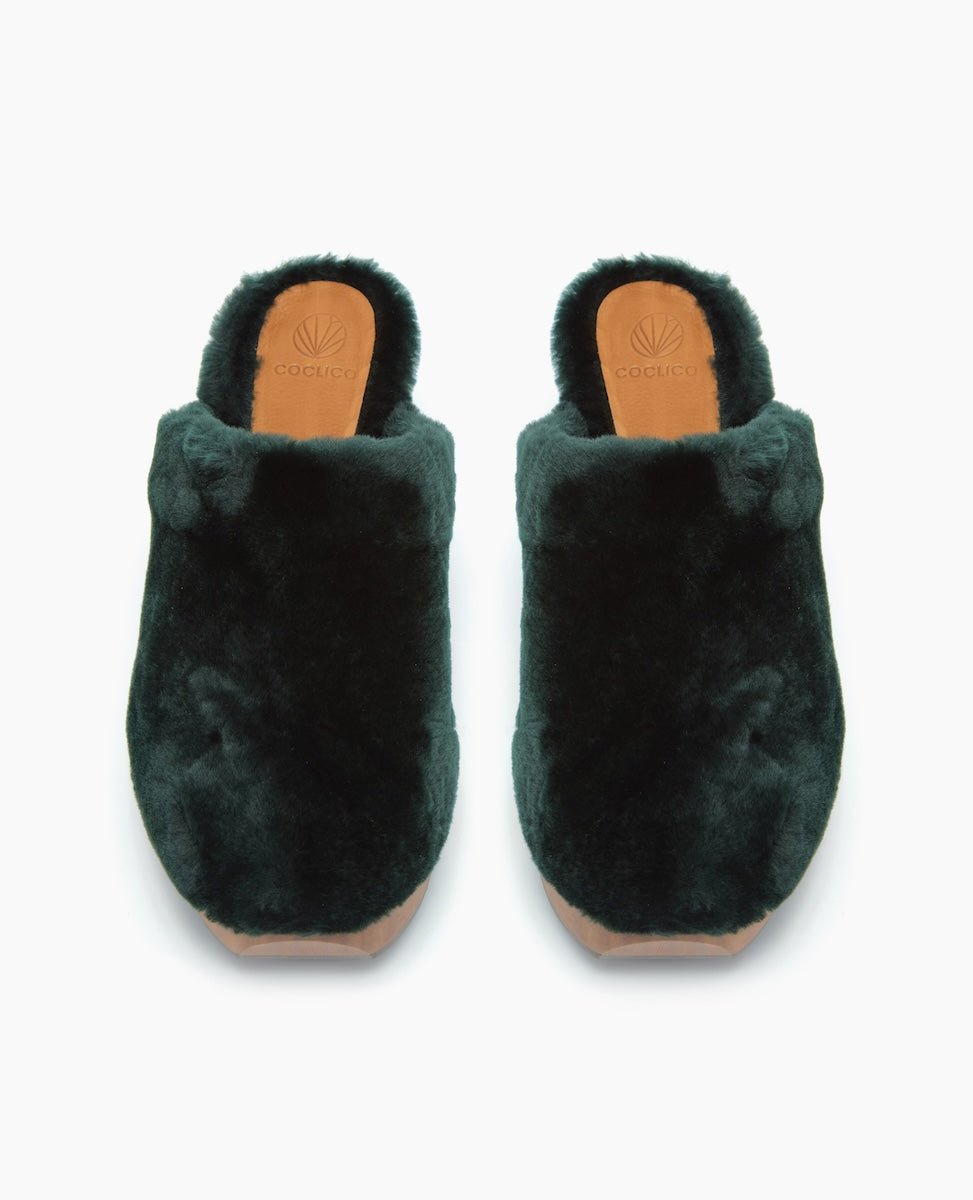 Dark green, plush, slip-on slippers with a soft, fuzzy texture, rounded toe, and a tan sole featuring a logo imprint.