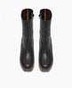 A pair of sleek, black leather ankle boots with a smooth texture, featuring a round toe, mid-calf height, and a contrasting brown sole with a subtle platform. 6