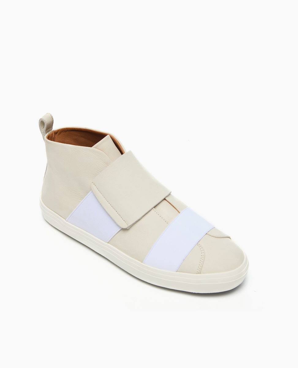 A sleek, high-top sneaker featuring a smooth, off-white leather exterior with wide white elastic bands across the top, a rounded toe, a pull tab at the heel, and a white rubber sole.