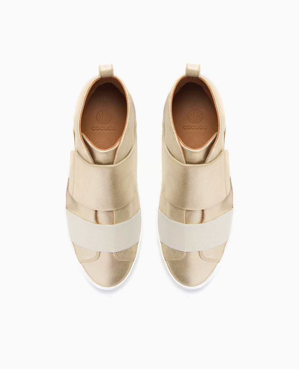 A pair of beige high-top sneakers with a smooth, matte finish, featuring wide elastic bands across the top, a pull tab at the heel, and a white rubber sole.