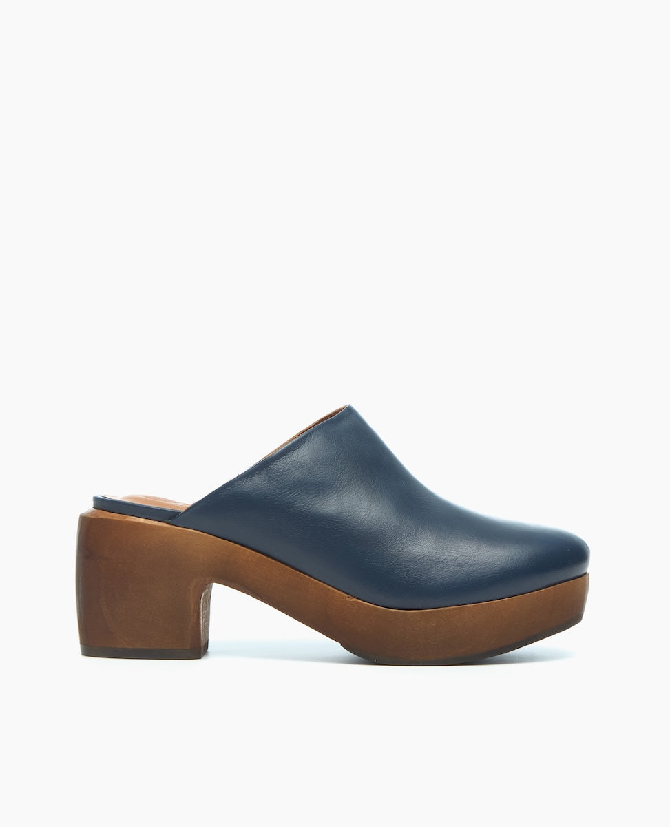 A blue leather clog with a smooth texture, featuring a closed toe, a chunky brown wooden platform heel, and an open back design.