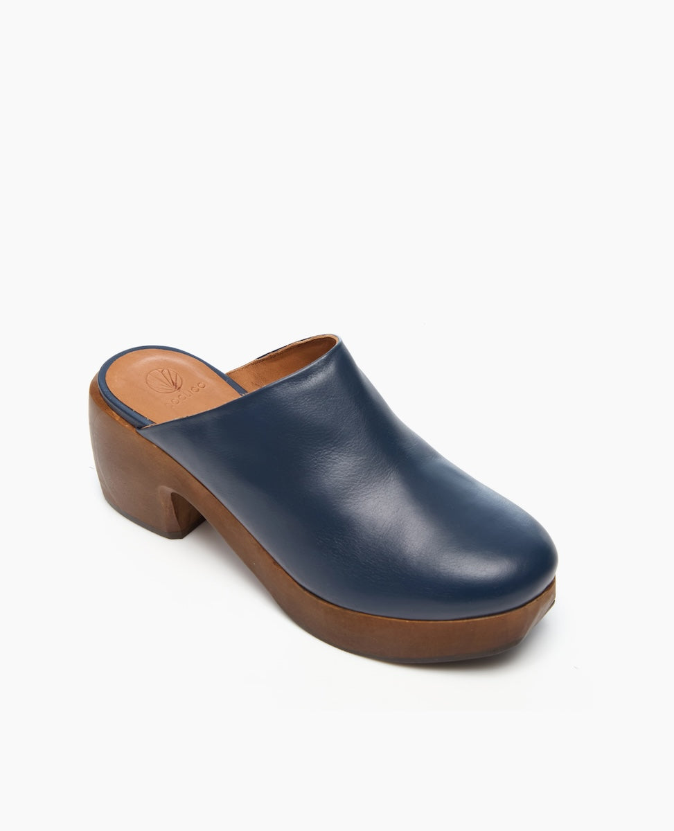 A blue leather clog with a smooth texture, featuring a rounded toe, a wooden platform sole, and a chunky heel.