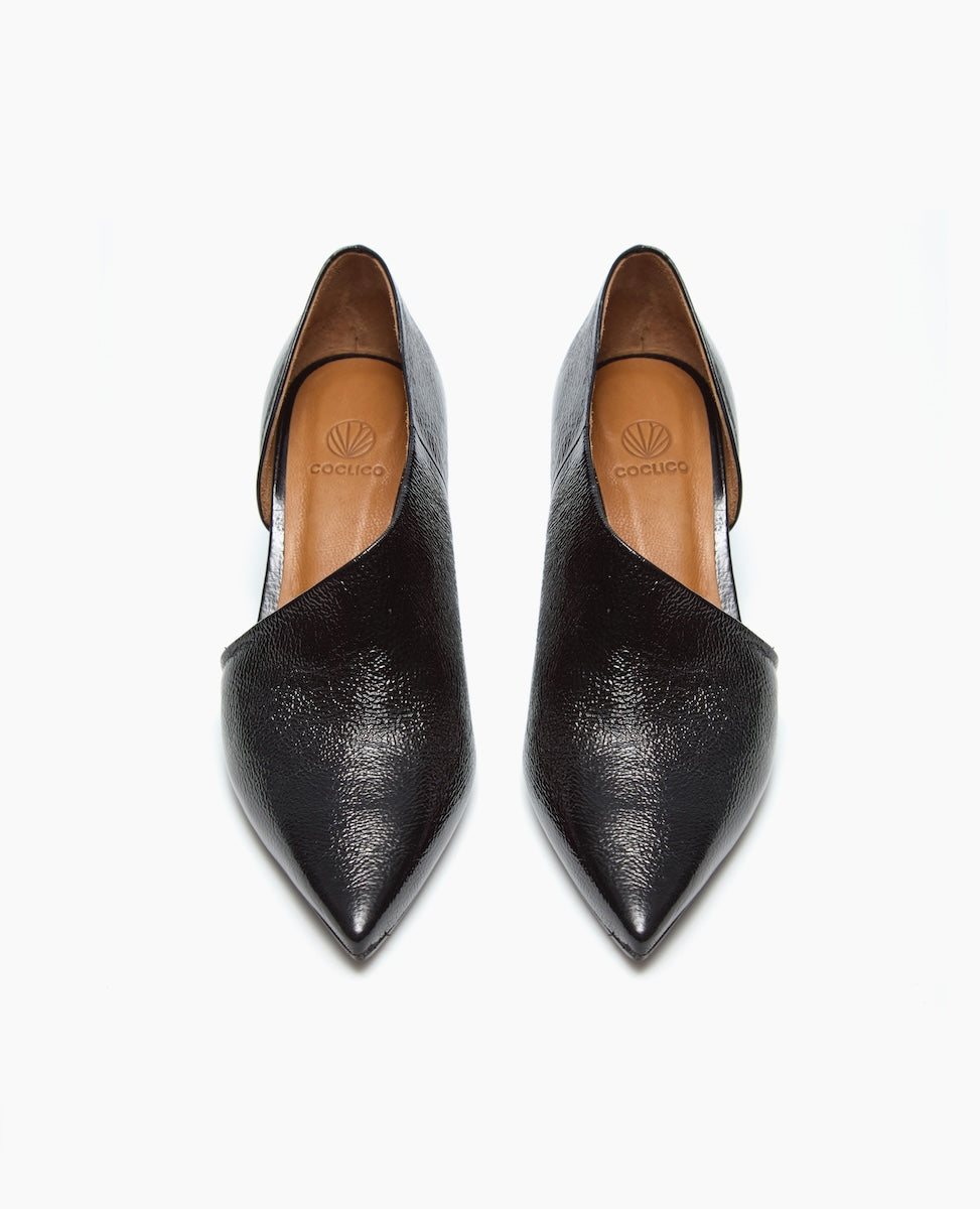 Black leather pointed-toe flats with a textured finish, asymmetrical v-cut design, and tan insoles featuring a logo.
