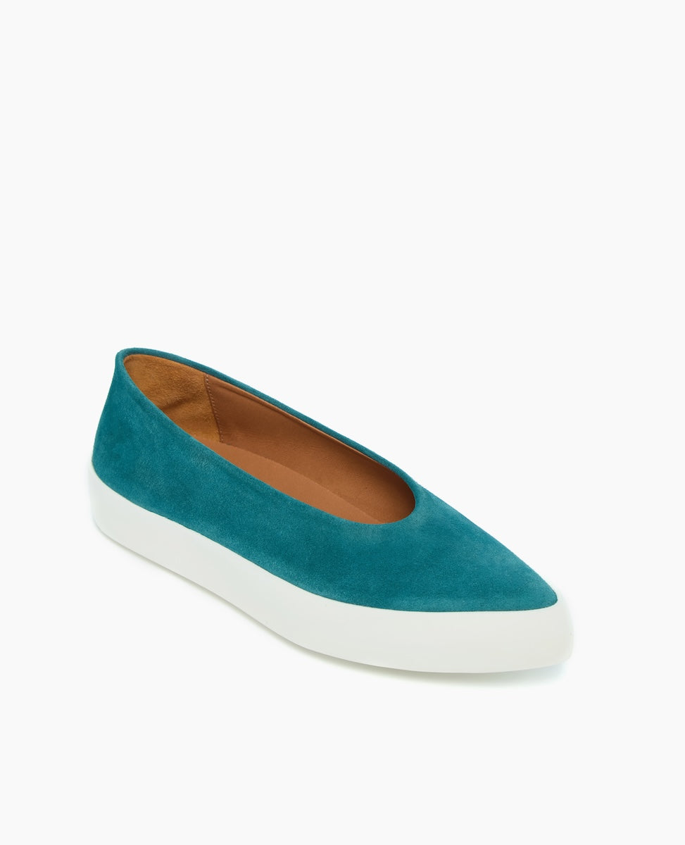 A teal suede slip-on shoe with a white rubber sole, featuring a rounded toe and a minimalist design.