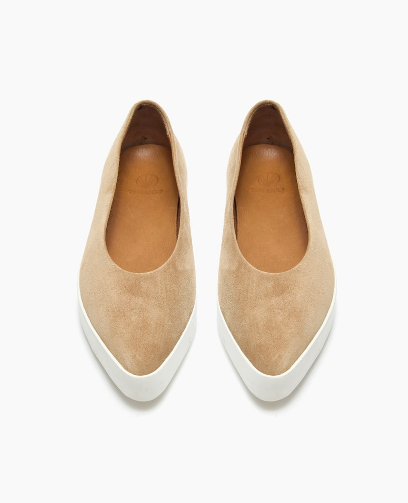 A pair of tan suede slip-on shoes with a smooth texture, rounded toes, white rubber soles, and a minimalist design.