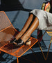 Woman's legs splayed out with feet resting on an orange chair an wearing the Sokolo Heel in Black Leather.  2