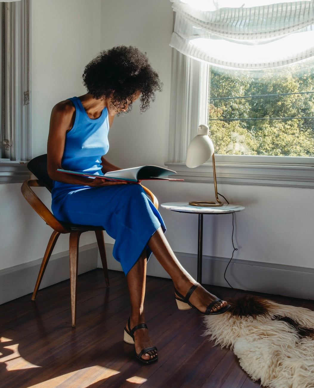 Woman seated on a chair looking through a book wearing a blue tank dress and the Sterling in Anthracite Shimmer Suede.