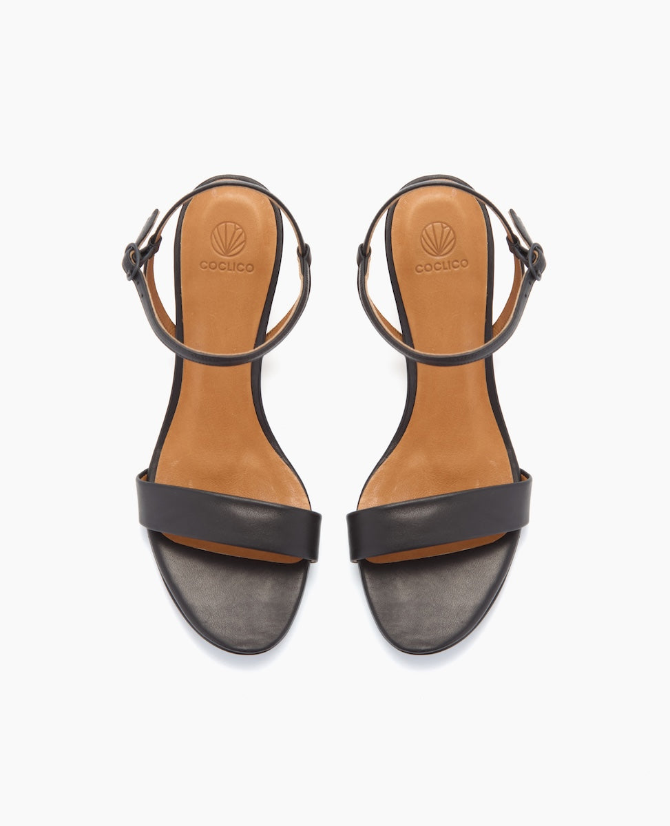 Black leather sandals with a tan insole, featuring a single front strap, an adjustable ankle strap with a buckle, and a flat sole.