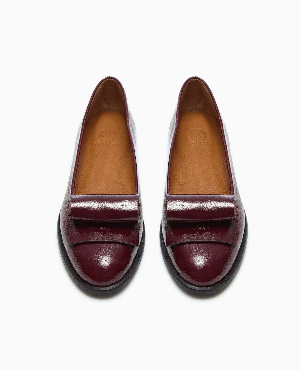 A pair of shiny, burgundy leather loafers with tan insoles and black soles, viewed from above.