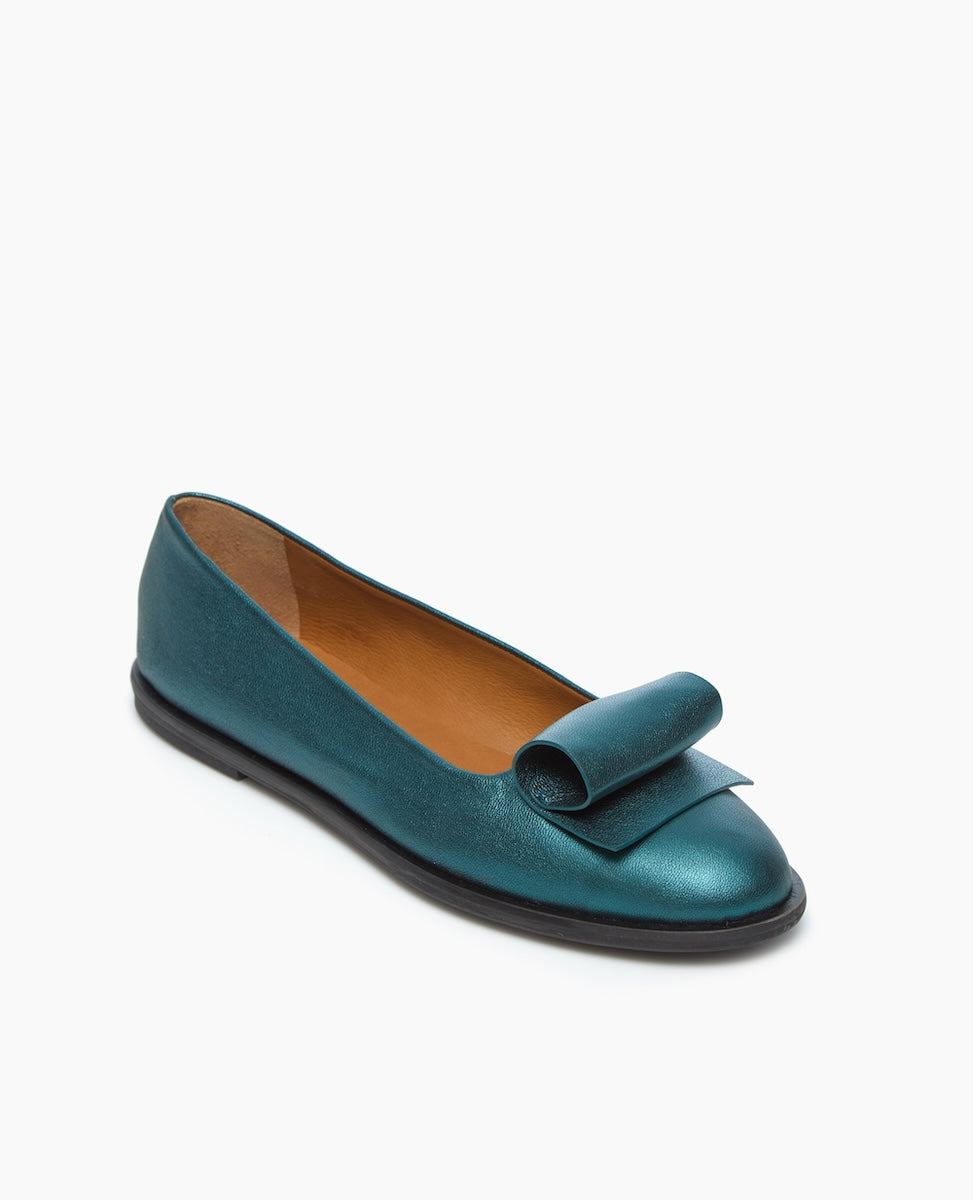 A teal-colored, slip-on flat shoe with a smooth, metallic finish, featuring an architectural loop detail on the front, a rounded toe, and a black sole.