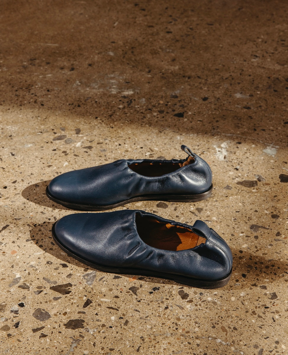 A pair of black leather slip-on shoes is placed on a textured concrete surface.