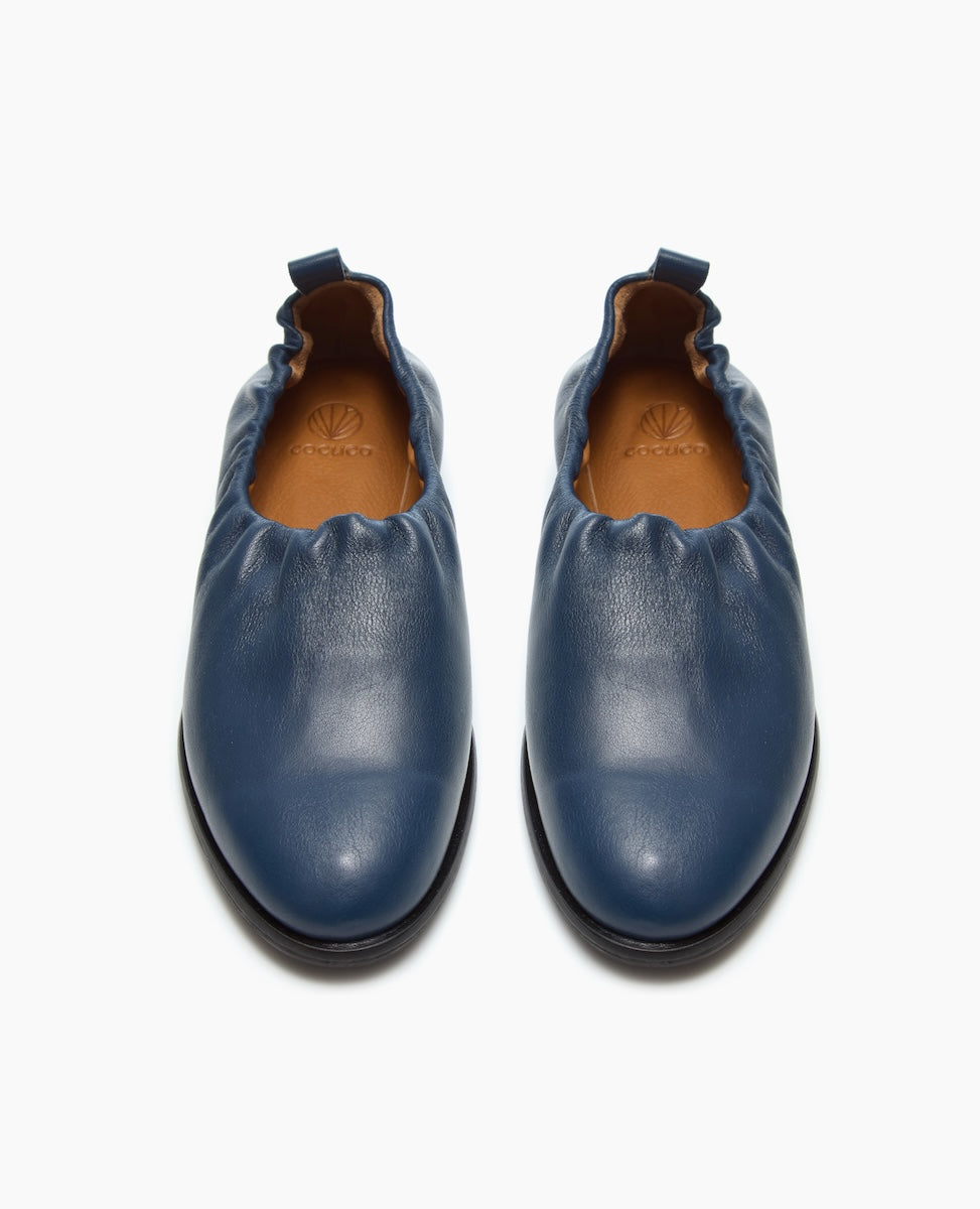 A pair of blue leather slip-on shoes with a gathered elastic top and a brown insole featuring a logo.