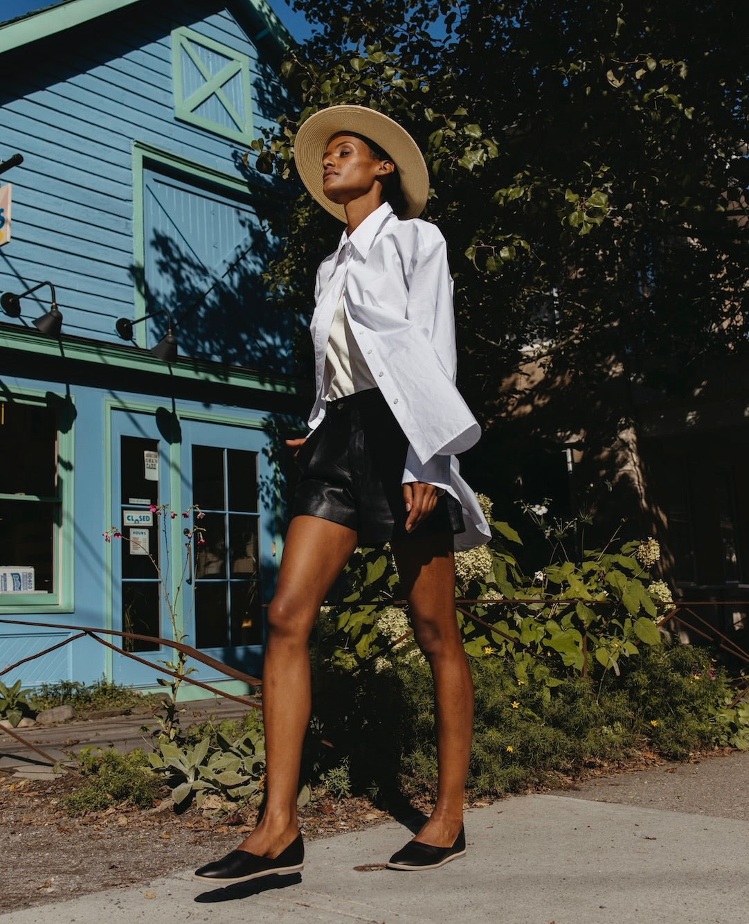 Woman walking outside wearing a white button down shirt with black leather pants and the Yen Flat in Black.