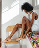 Woman sitting down on a bench placing the right pair of the Yen Flat in Faun on. 2