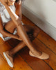 Woman sitting on the floor with her legs crossed wearing the Yen Flat in Faun. 4