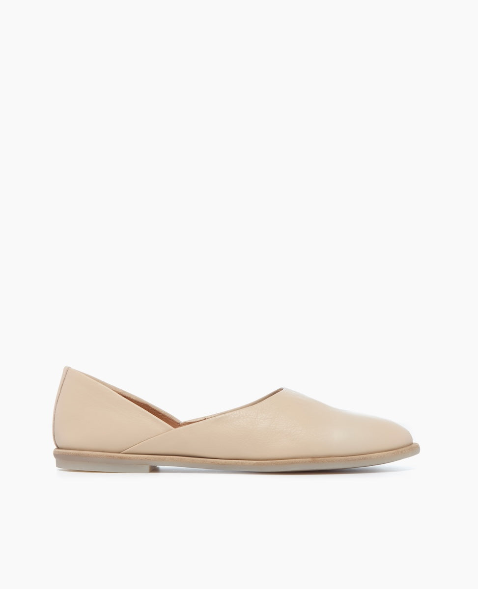 A beige, slip-on flat shoe with a smooth leather texture, featuring a slightly pointed toe and a low, flat heel.