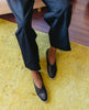 Legs and feet of a woman against a yellow rug wearing black pants and the Yoko Flat in Deep Sea. 4