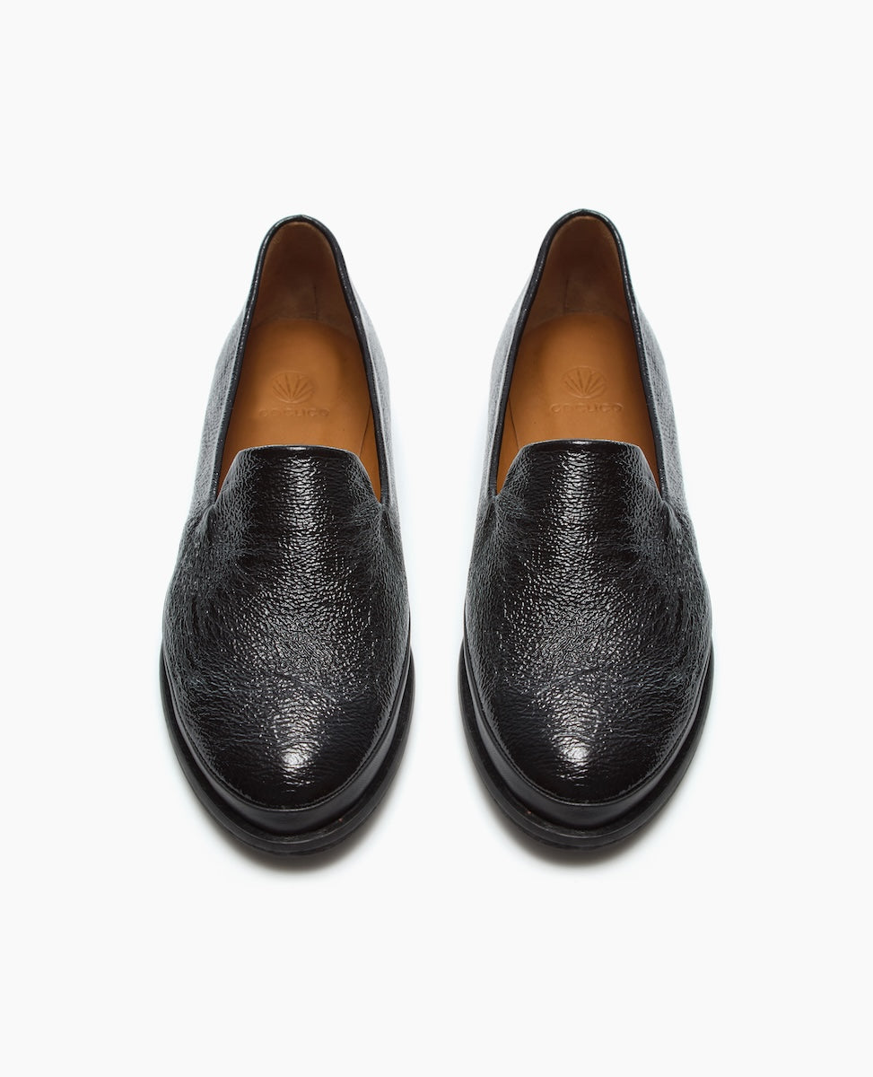 A pair of black leather slip-on shoes with a textured finish, rounded toes, and tan-colored insoles.