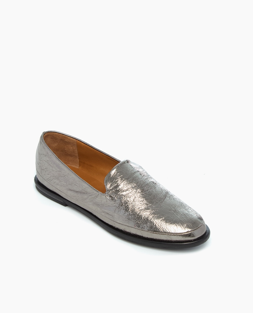A sleek, metallic silver loafer with a smooth, shiny texture, featuring a low heel, rounded toe, and a subtle embossed pattern on the upper material.