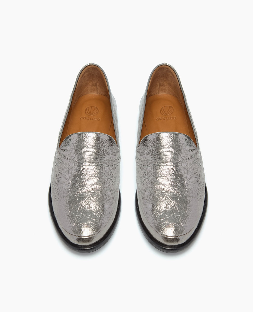 Silver metallic loafers with a textured, crinkled surface, featuring a rounded toe, low black heel, and tan leather interior.